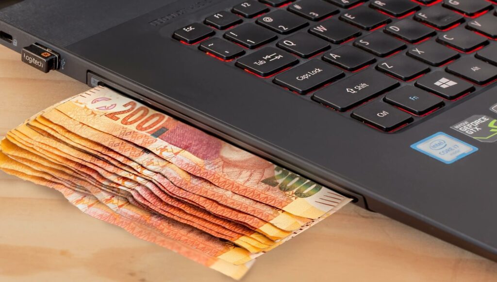 mehrere 200 € Scheine liegen halb unter Laptop - Symbolbild für Betrug wegen Corona Soforthilfe